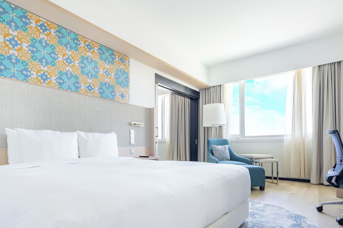 Une chambre d’hôtel avec un grand lit, un bureau, une chaise et une vue sur le ciel par la fenêtre.