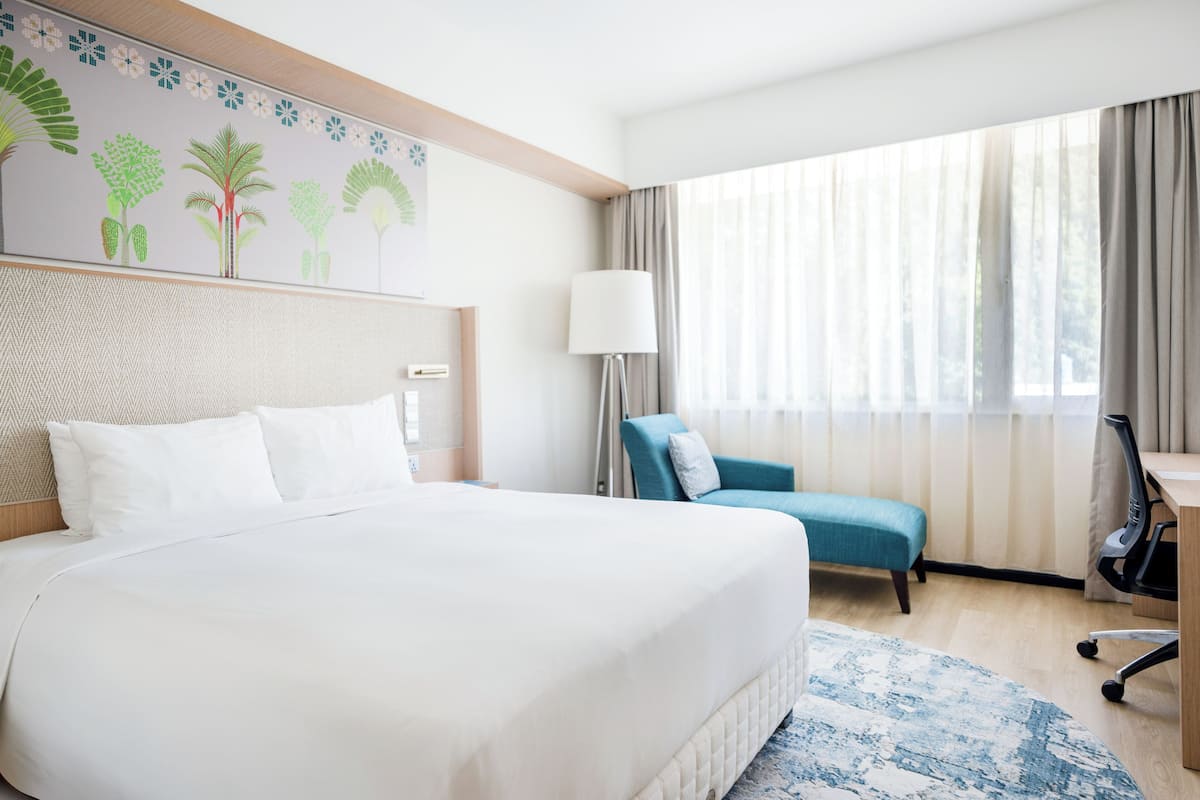 Une chambre d’hôtel avec un grand lit, un bureau, une chaise, une lampe et une fenêtre avec des rideaux.