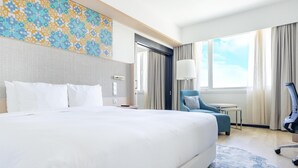 Una habitación de hotel con una cama grande, un escritorio, una silla y vistas al cielo a través de la ventana.