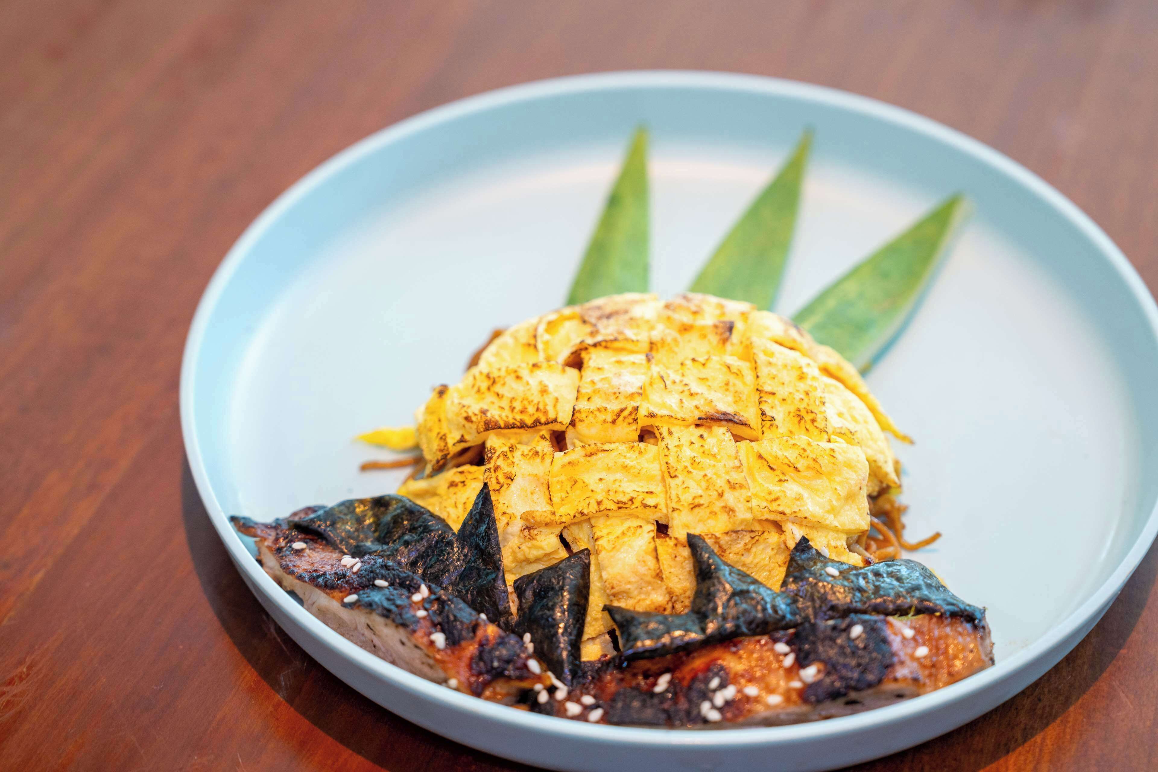 Une assiette avec du poisson grillé et un œuf grillé, le tout servi sur une assiette bleue.