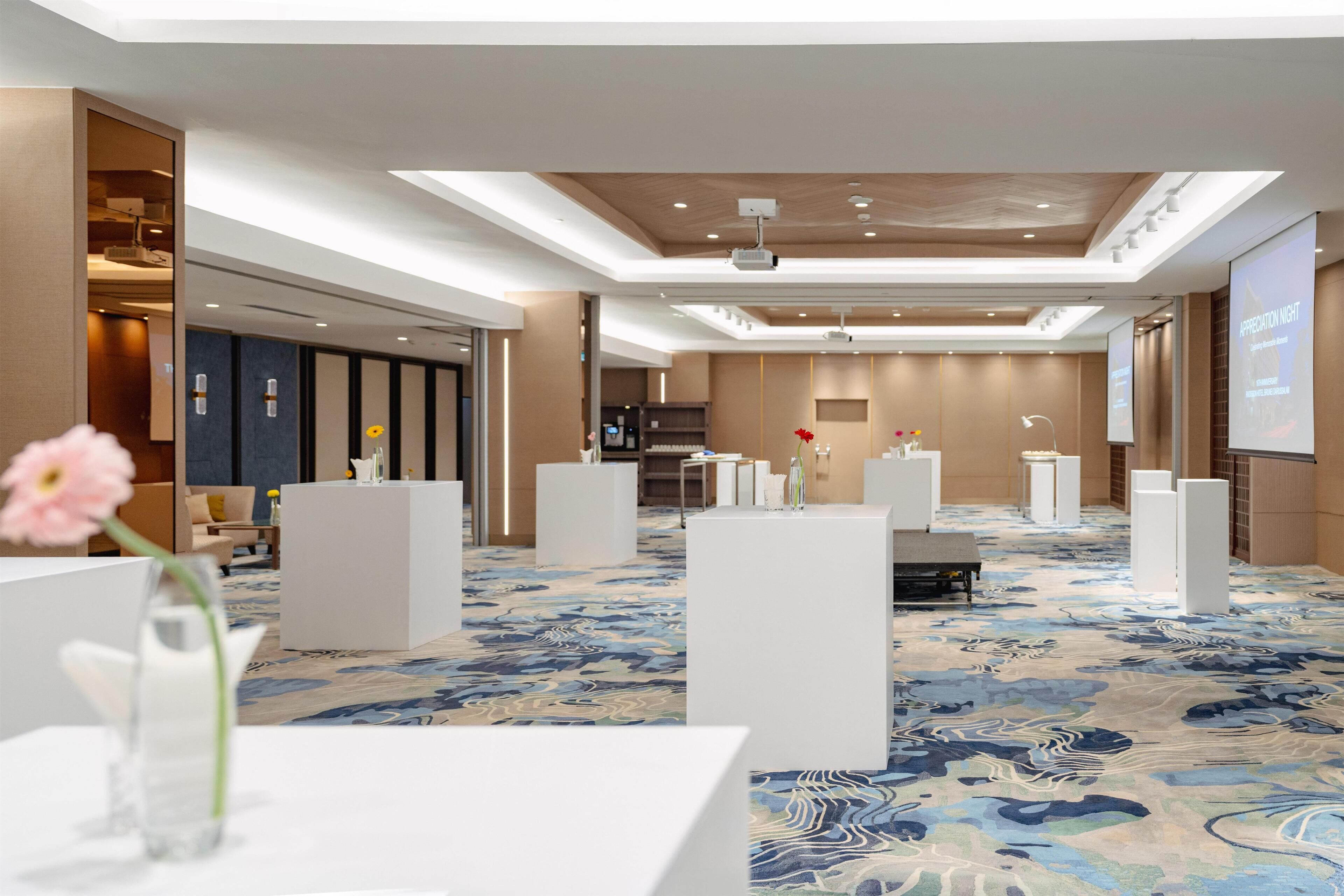 A hotel lobby with a modern design, featuring a large carpeted area, white reception counters, and a projection screen displaying 'APPRECIATION NIGHT'.