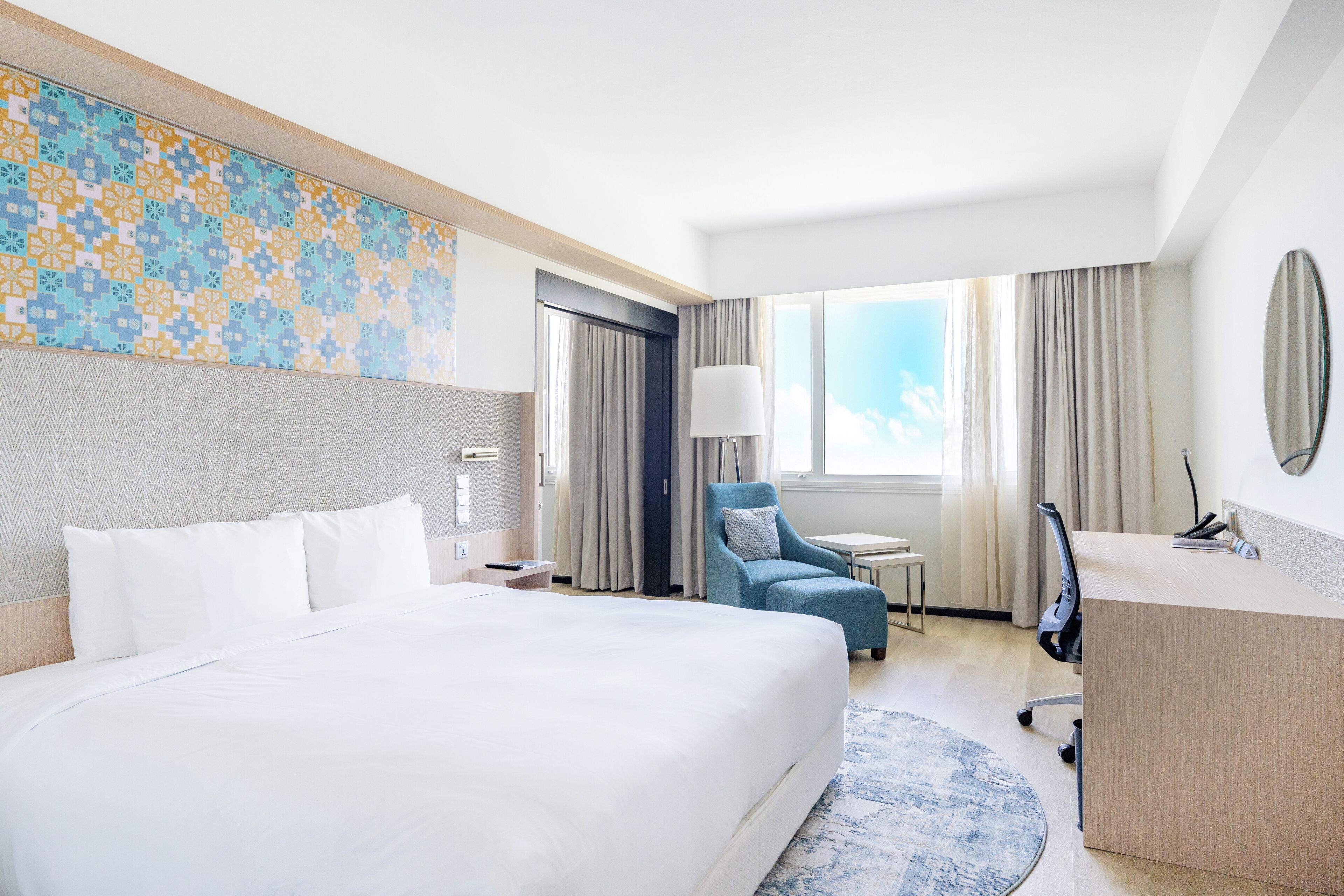 Habitación de hotel con una cama grande, un escritorio, una silla, una lámpara y vistas al cielo.