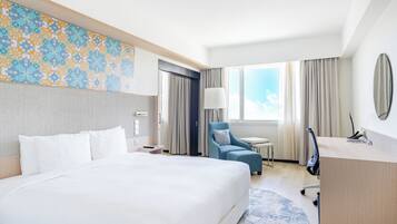 Habitación de hotel con una cama grande, un escritorio, una silla, una lámpara y vistas al cielo.