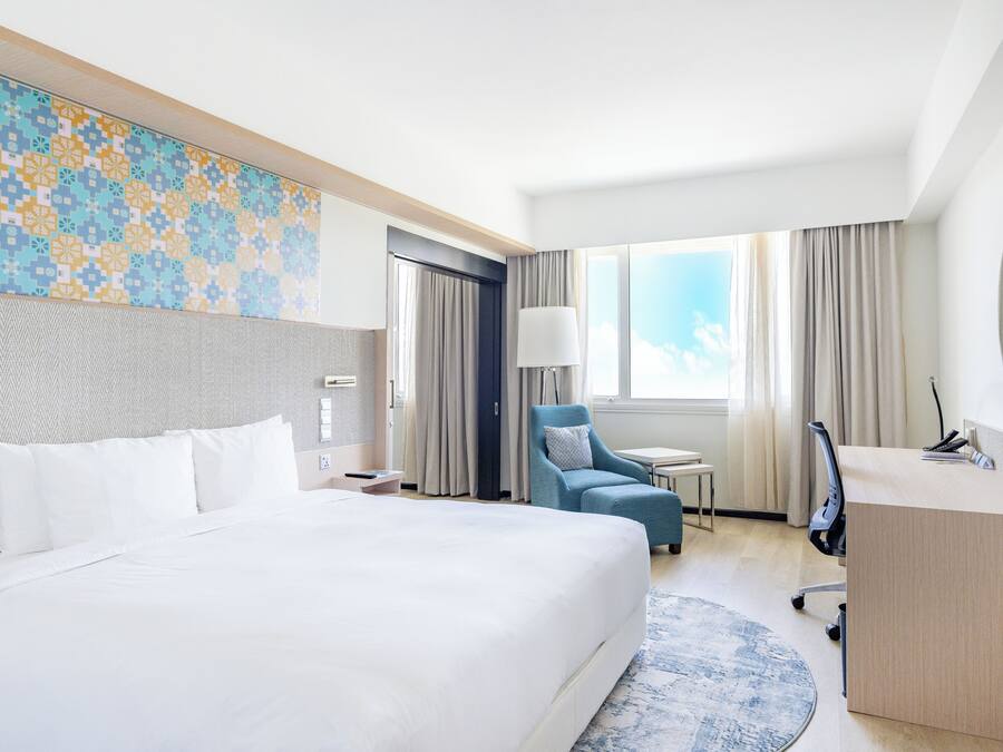 Habitación de hotel con una cama grande, un escritorio, una silla, una lámpara y vistas al cielo.