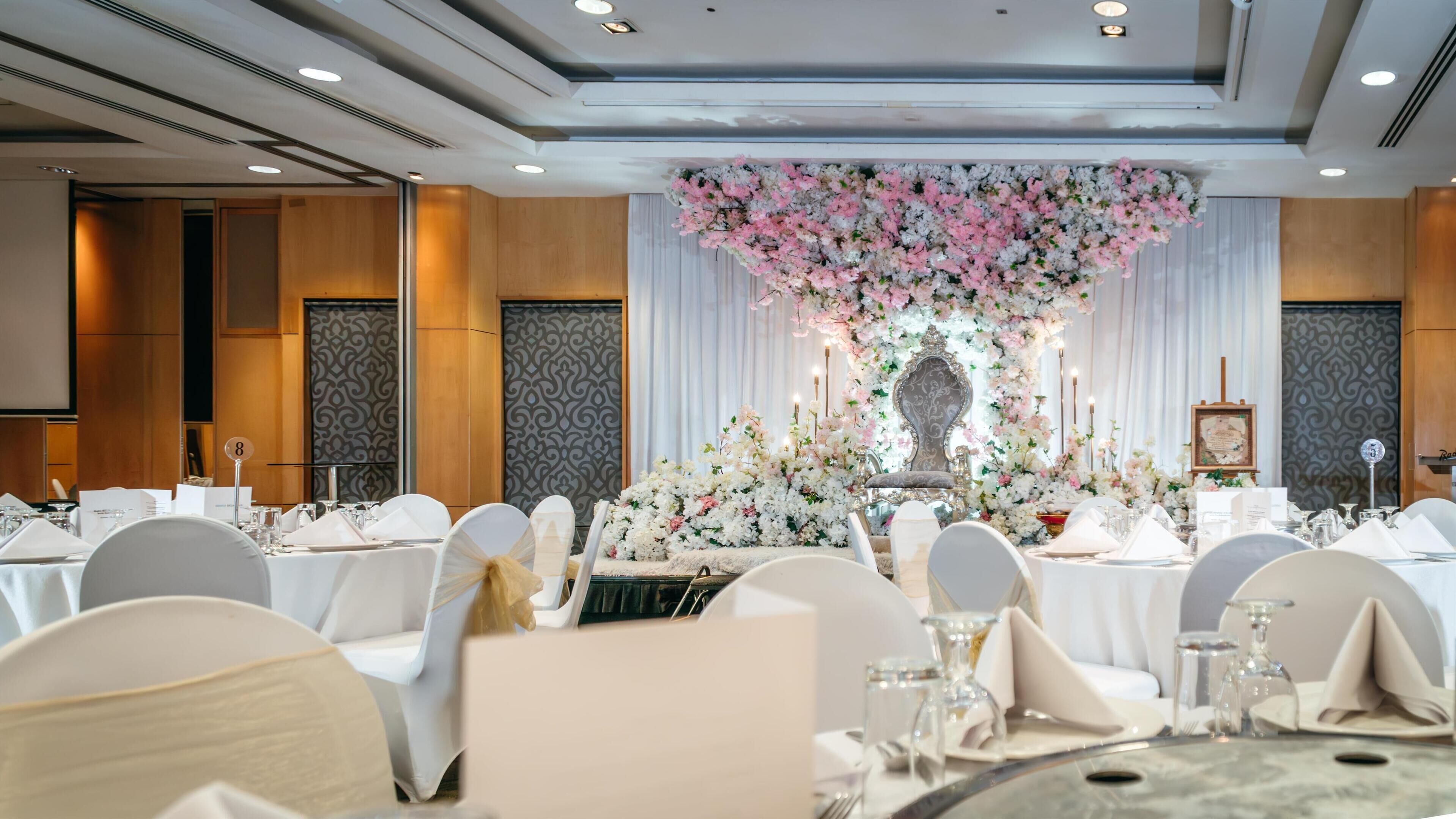 A banquet hall with round tables set for a formal event, featuring a floral centerpiece and elegant table settings.