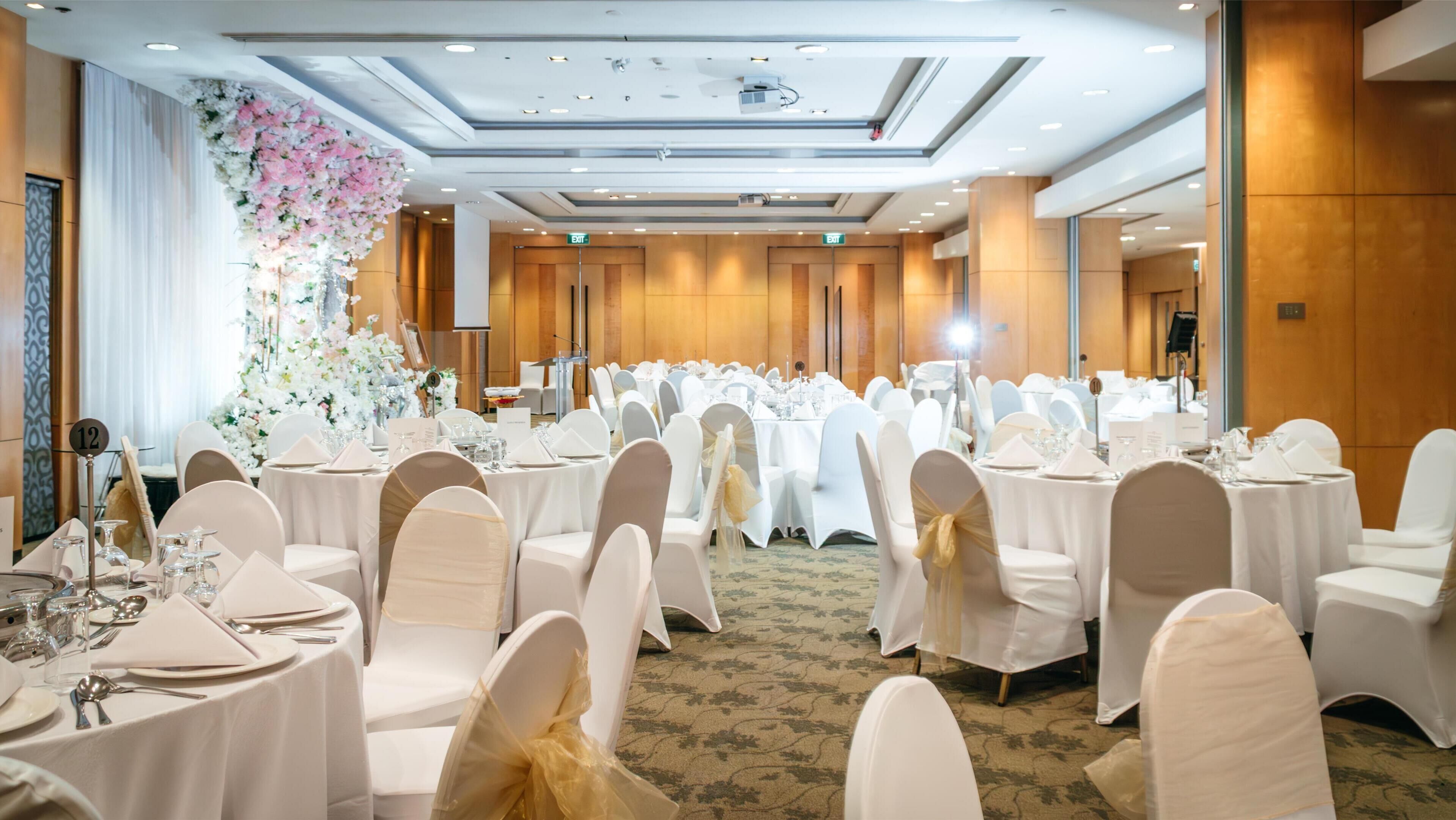 A banquet hall with round tables, white chairs, and floral decorations.