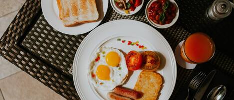 Una mesa de desayuno con tostadas, huevos, salchichas, tomates y un vaso de jugo de naranja.