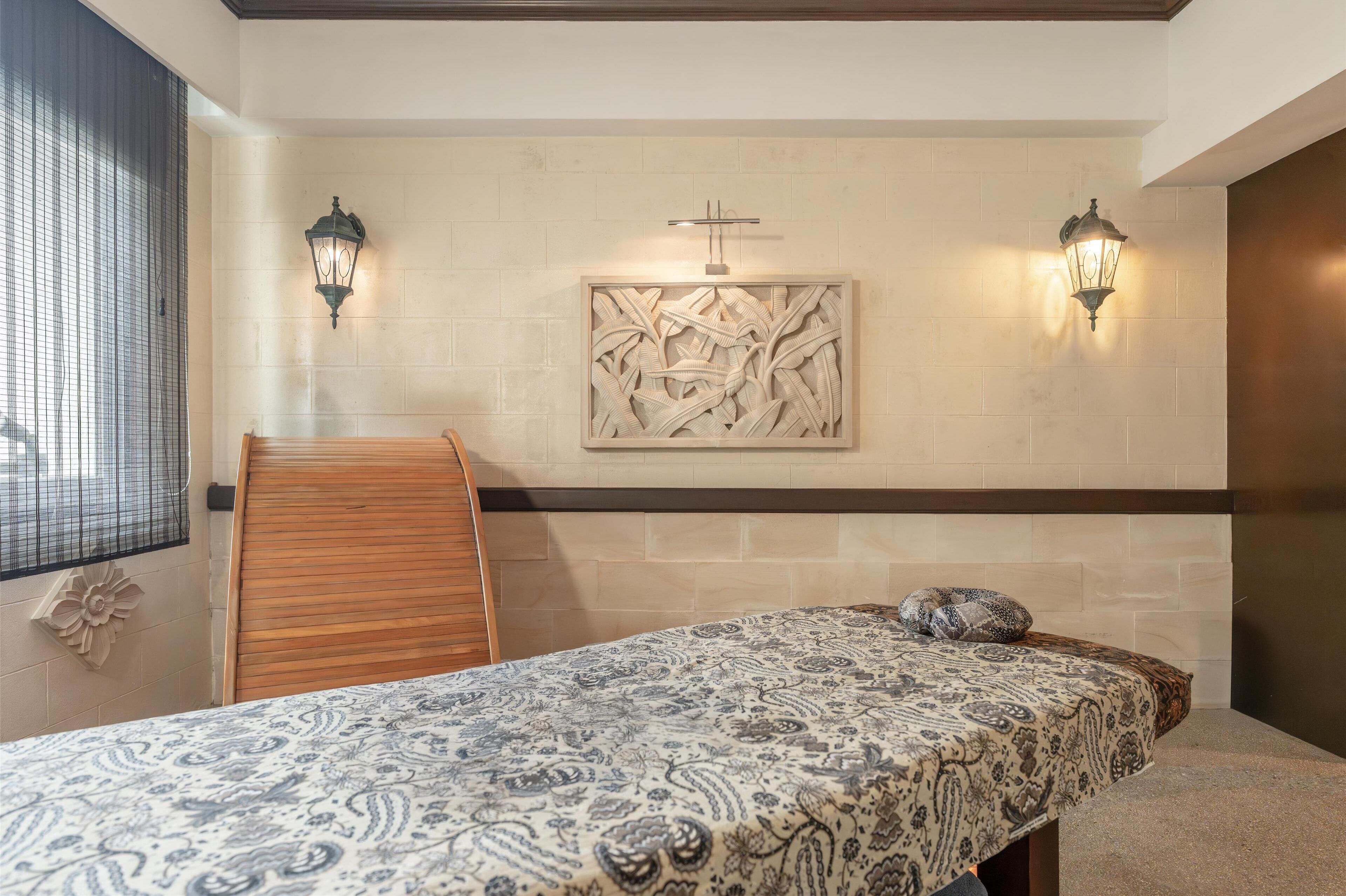 A room with a bed, a wooden chair, two wall-mounted lamps, and a decorative wall piece.