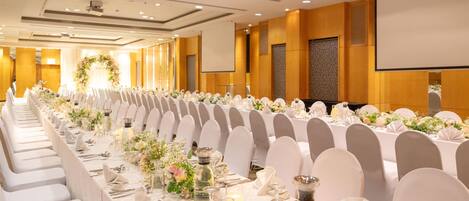 Una larga mesa de banquete dispuesta con manteles blancos, sillas y centros de mesa florales.