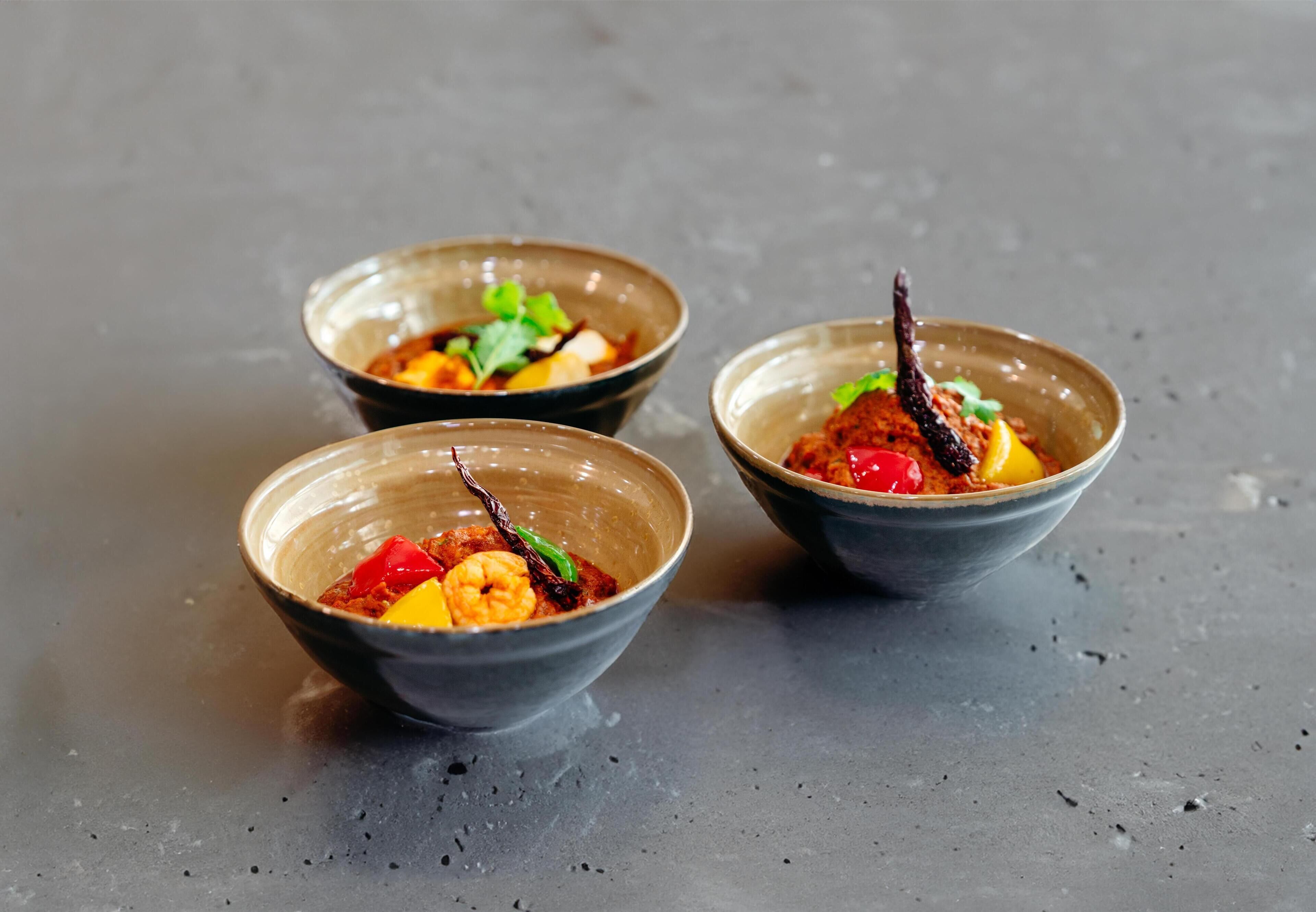 Three bowls of food on a dark surface.