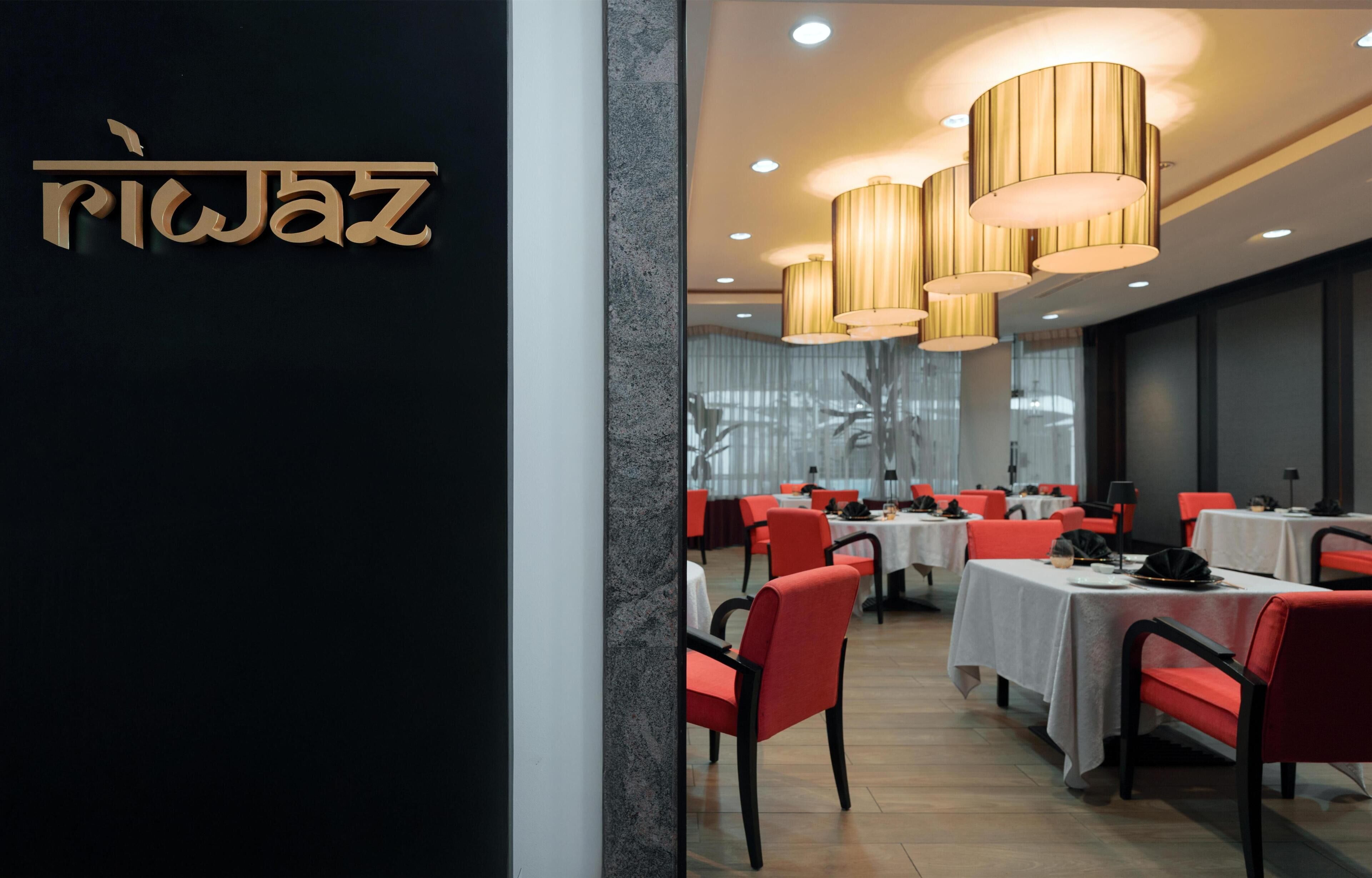 A restaurant interior with red chairs, white tables, and multiple hanging light fixtures.