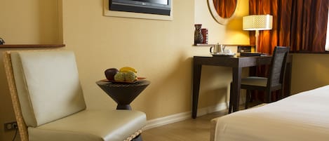Une chambre d’hôtel avec un lit, une chaise, une petite table avec des fruits, une lampe et un téléviseur fixé au mur.