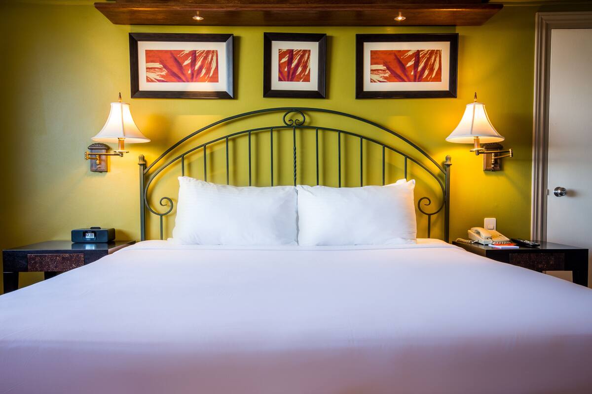 A neatly made bed with white linens, two bedside lamps, and a wall-mounted clock.