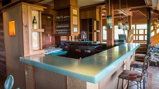 A bar area with a long counter, multiple seating options, and a variety of glassware displayed on shelves. - Kapok Hotel (Port of Spain)