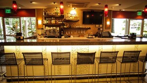 A bar area with a counter, bar stools, shelves with bottles, a TV, and exit signs. - Kapok Hotel (Port of Spain)