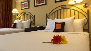 A hotel room with two beds, each with white linens and decorative pillows. There are wall-mounted lamps and framed artwork above the beds. - Kapok Hotel (Port of Spain)