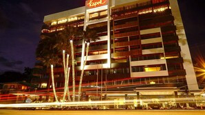 A multi-story hotel with a prominent 'Kapok' sign, featuring balconies and illuminated windows. - Kapok Hotel (Port of Spain)