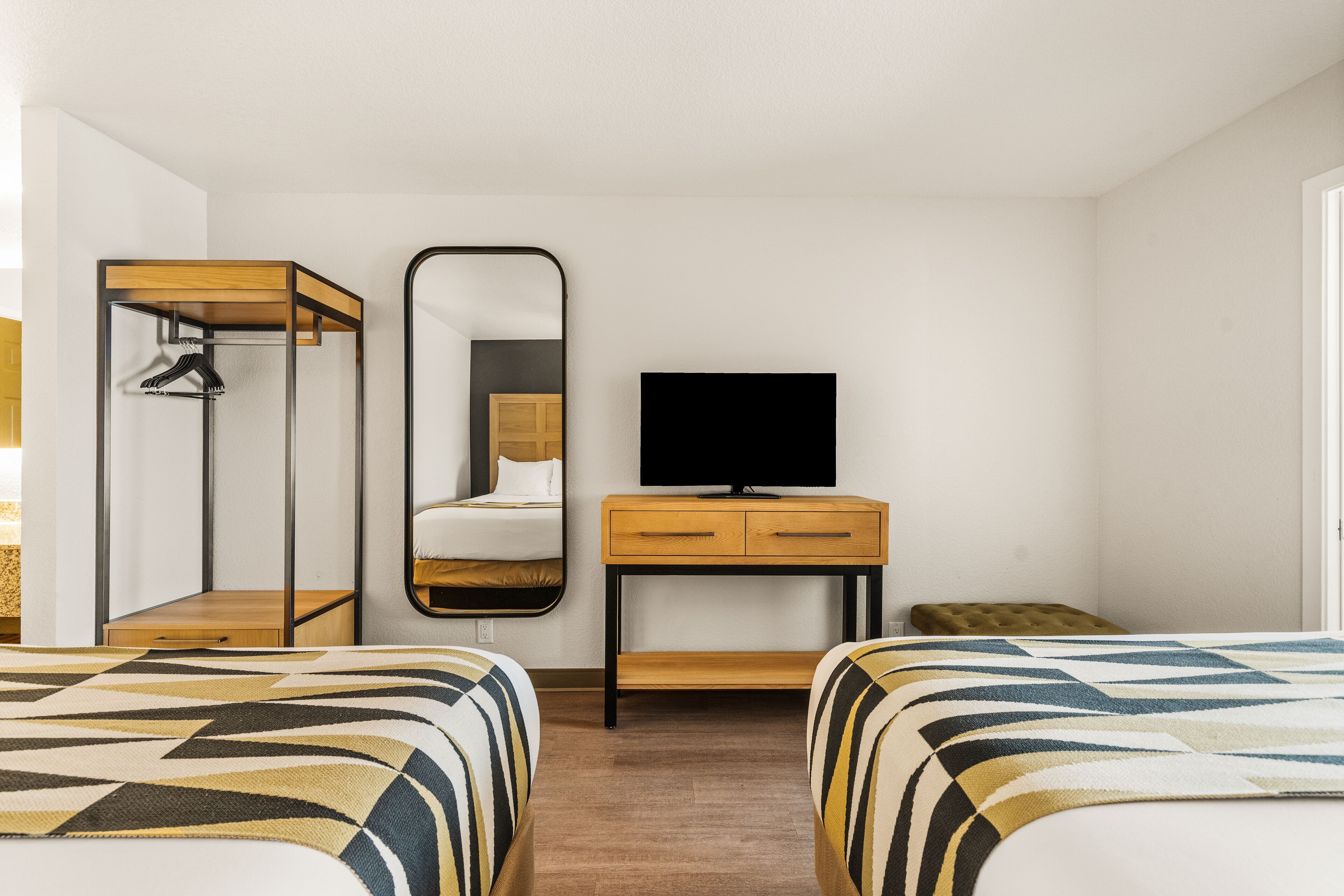 A hotel room with two beds, a TV, a mirror, a wardrobe, and a small table.