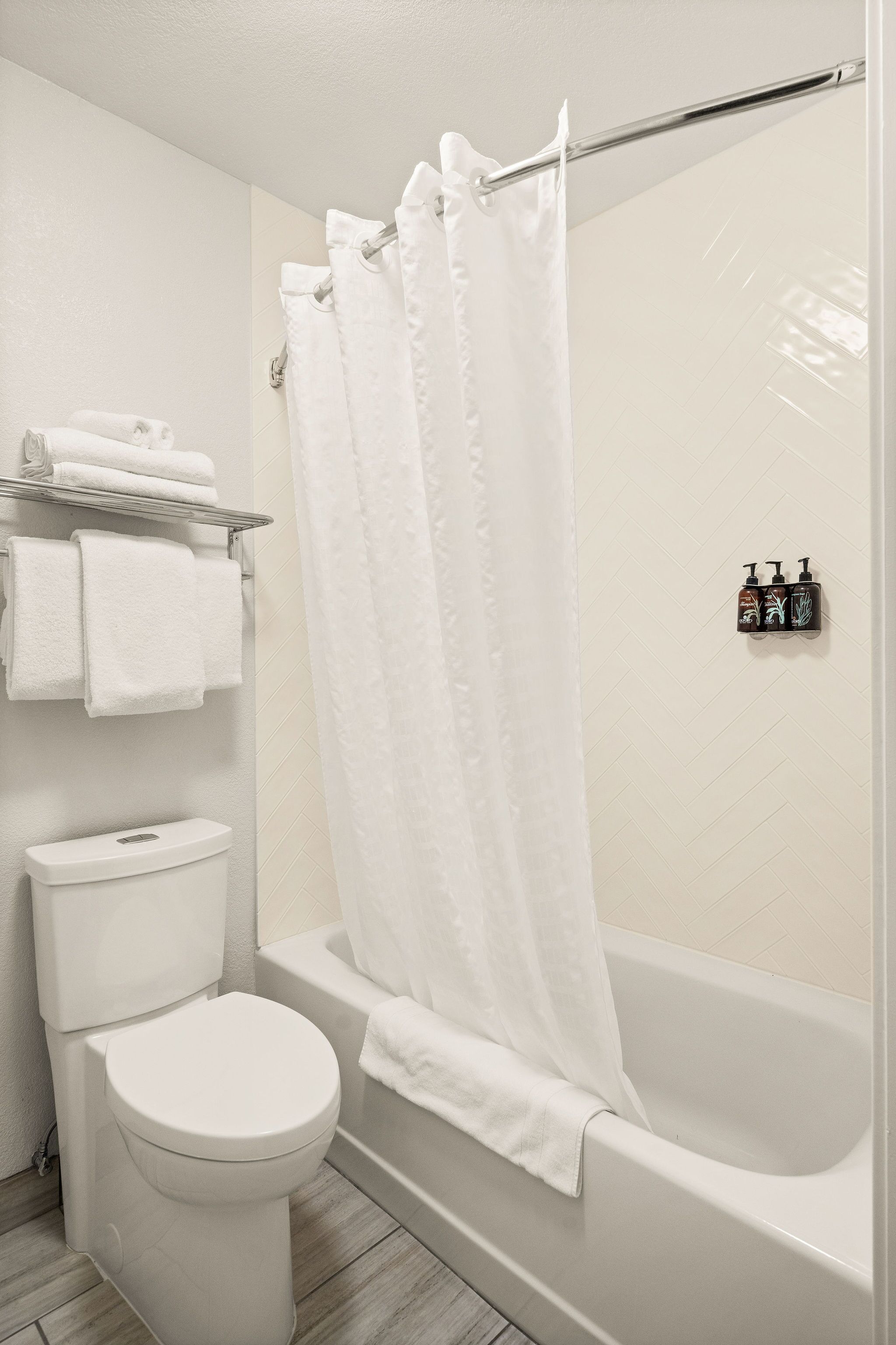 A bathroom with a white toilet, a bathtub, and a shower curtain. There are towels on a shelf above the toilet.