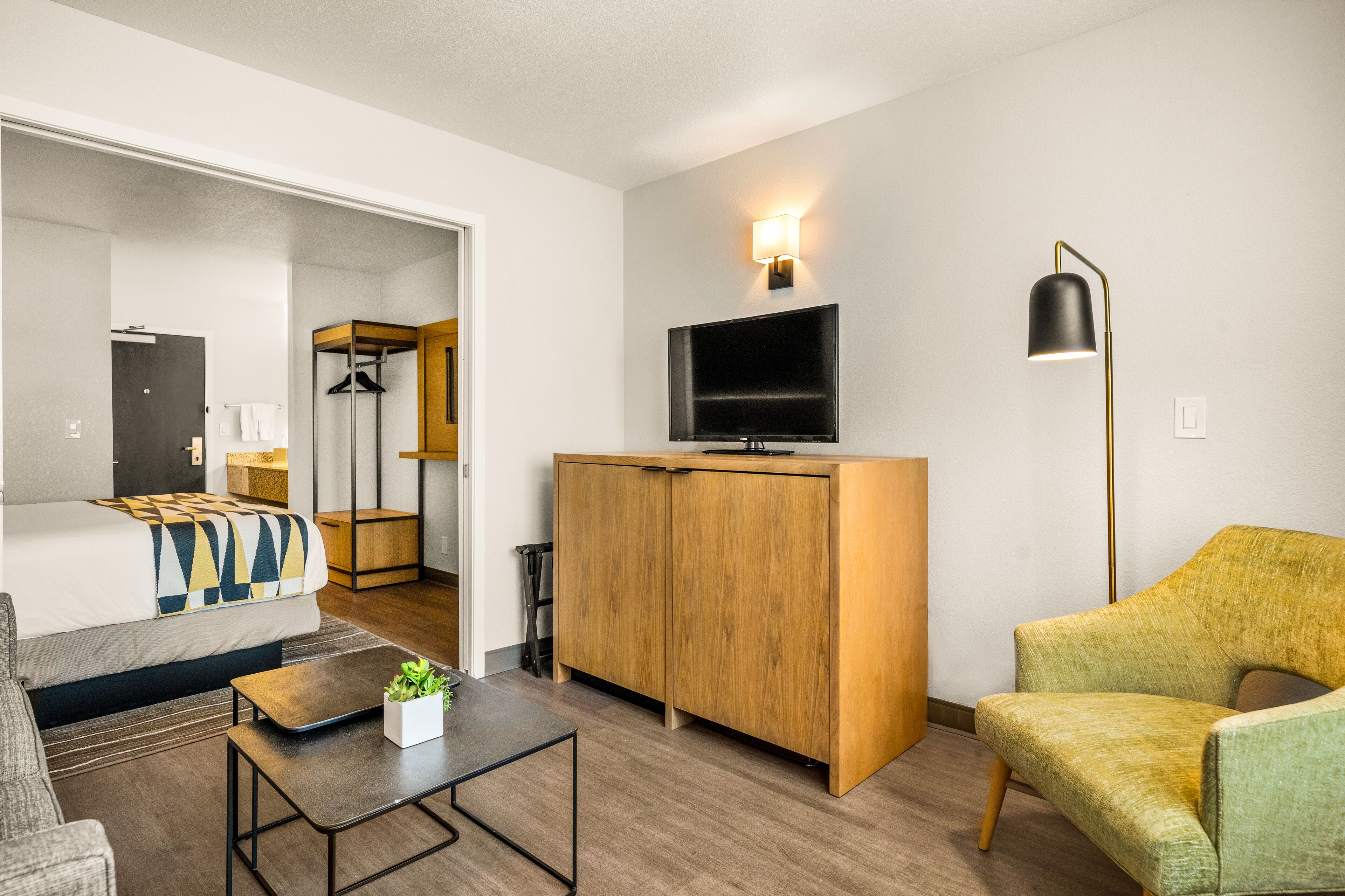 A modern hotel room with a bed, a sofa, a desk, a TV, and a chair.