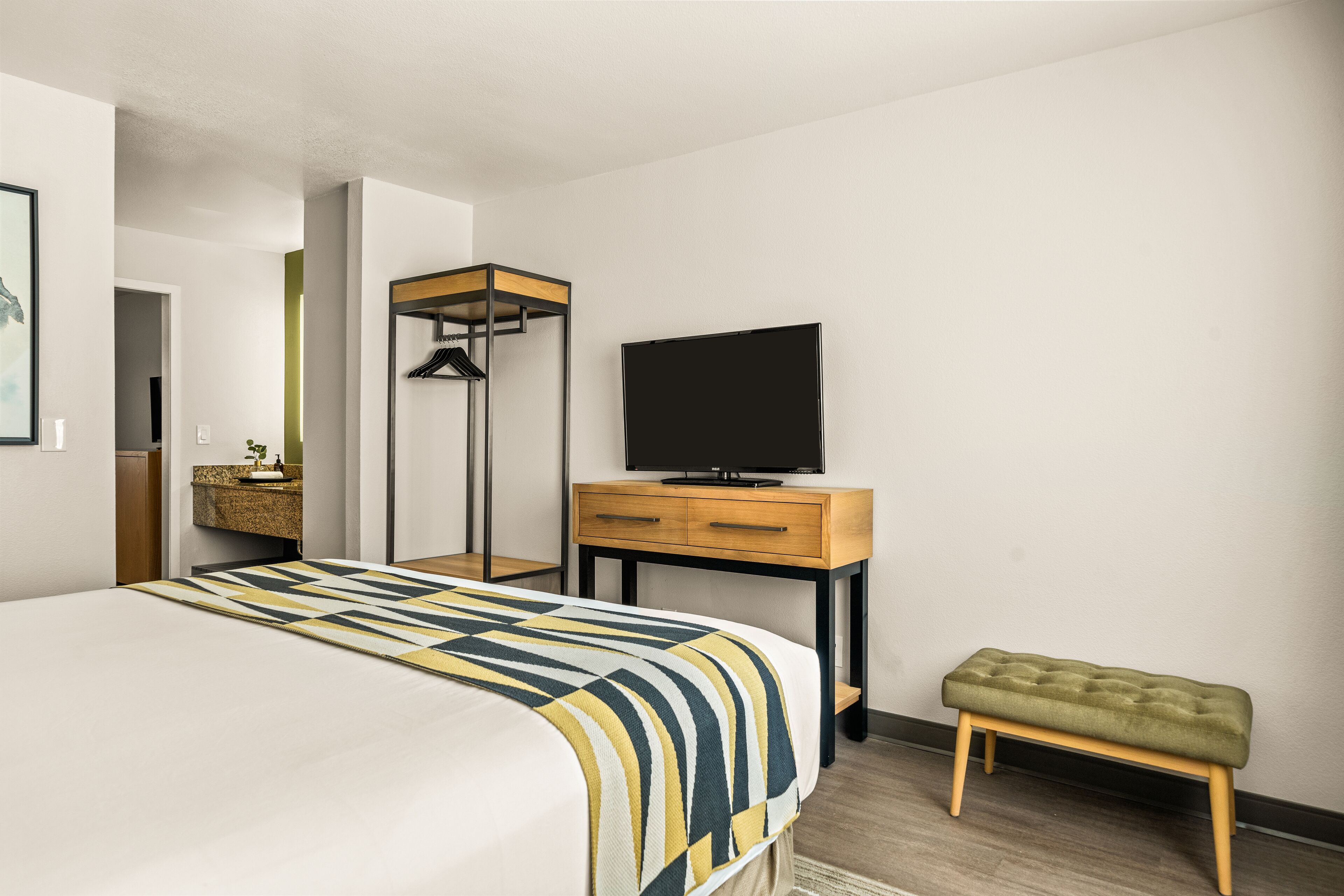 Una habitación de hotel moderna con una cama grande, una mesita de noche de madera con un televisor, un banco y un armario.