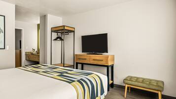 Una habitación de hotel moderna con una cama grande, una mesita de noche de madera con un televisor, un banco y un armario.
