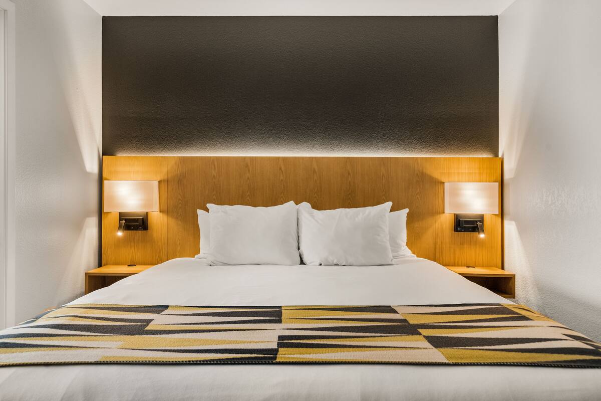 A neatly made bed with a patterned bedspread, a wooden headboard, and two bedside lamps.