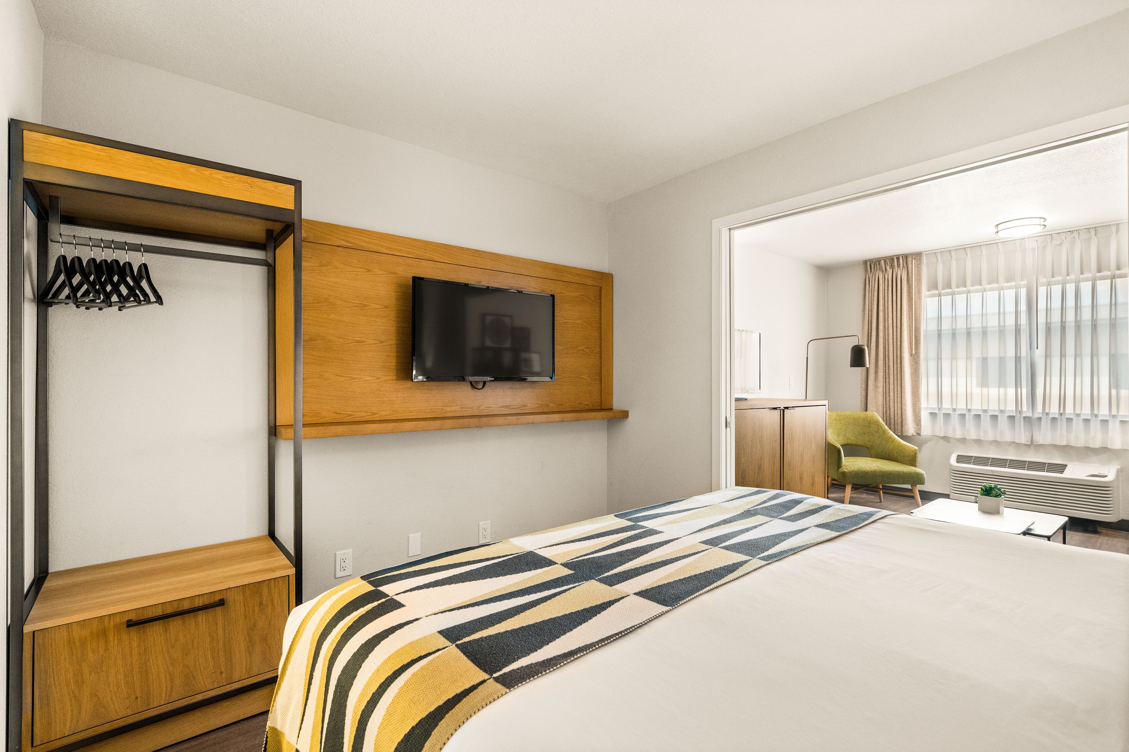 A hotel room with a bed, a TV mounted on the wall, a wardrobe, and a chair.
