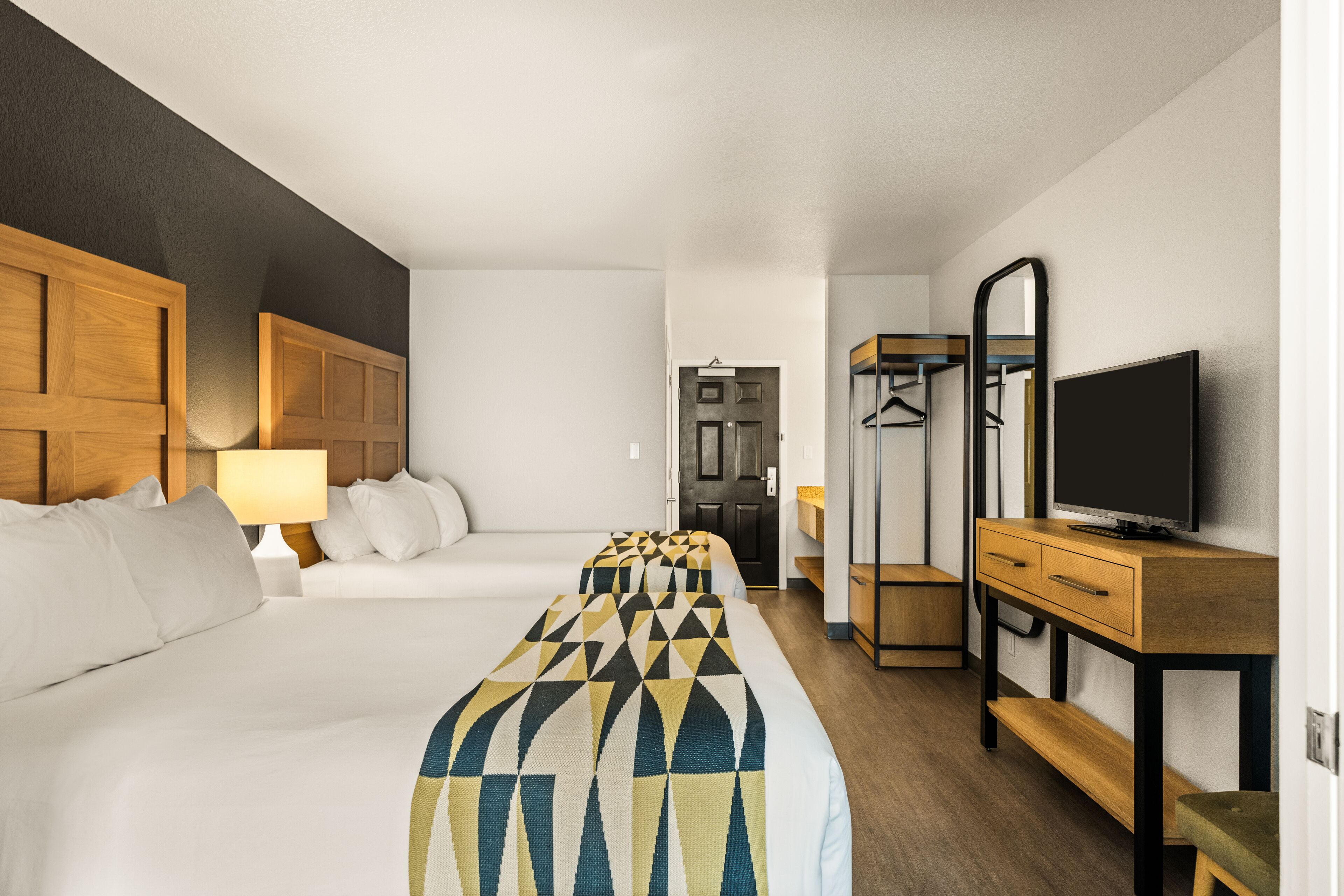 A hotel room with two beds, a TV, a mirror, and a wooden dresser.