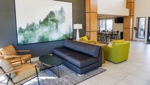 Un hall d’entrée moderne agrémenté d’un grand tableau abstrait, d’un canapé gris foncé, d’une chaise en bois, d’une petite table ronde et d’un fauteuil vert vif.