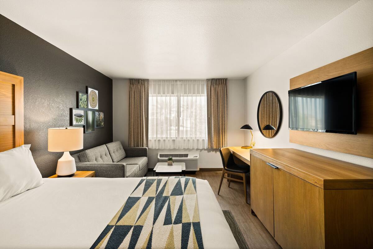 A hotel room with a bed, a desk, a chair, a TV, and a wardrobe.