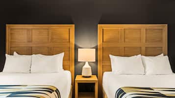 Habitación de hotel con dos camas, una mesita de noche con lámpara y una pared oscura.