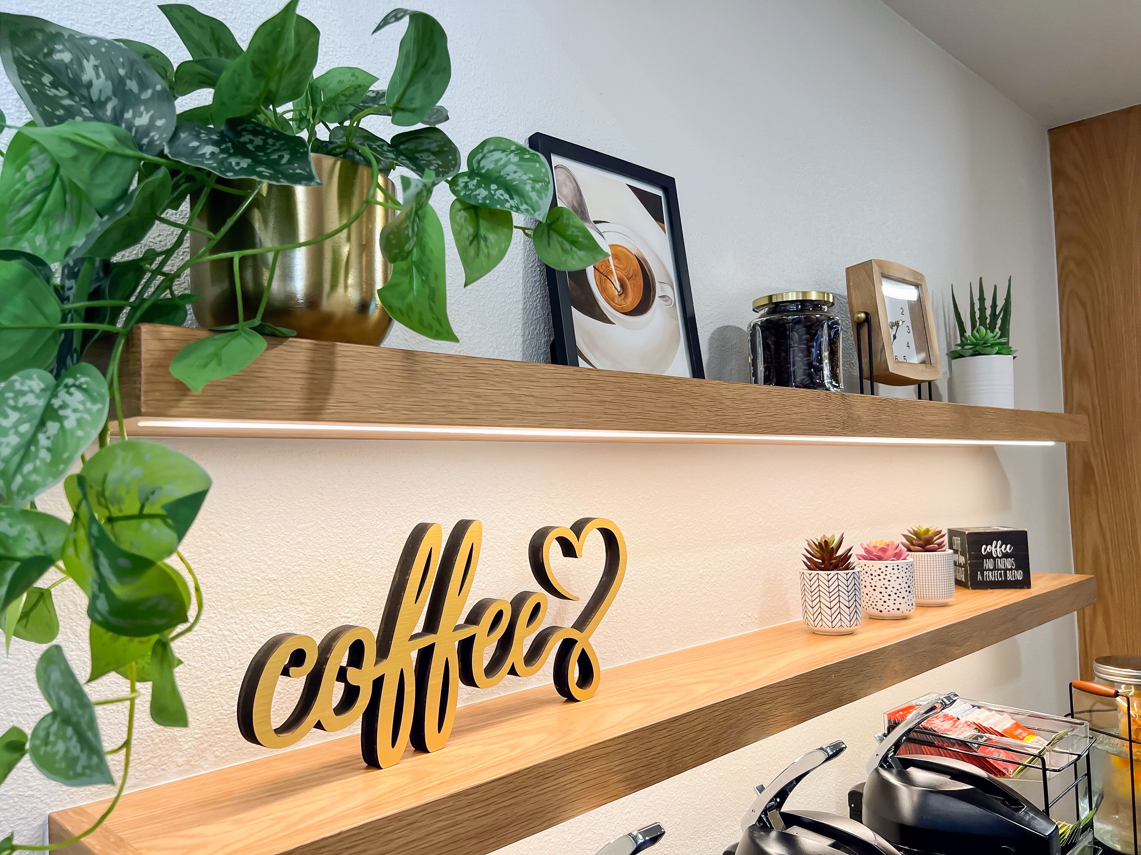 Una estantería con un letrero con temática de café, una cafetera y diversas plantas.