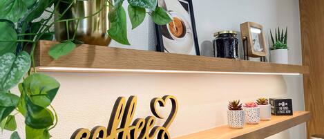 Una estantería con un letrero con temática de café, una cafetera y diversas plantas.
