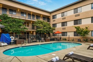 A hotel with a swimming pool, outdoor seating, and a covered area with a grill.