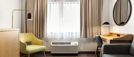 A modern living room with a sofa, armchair, desk, and air conditioning unit.