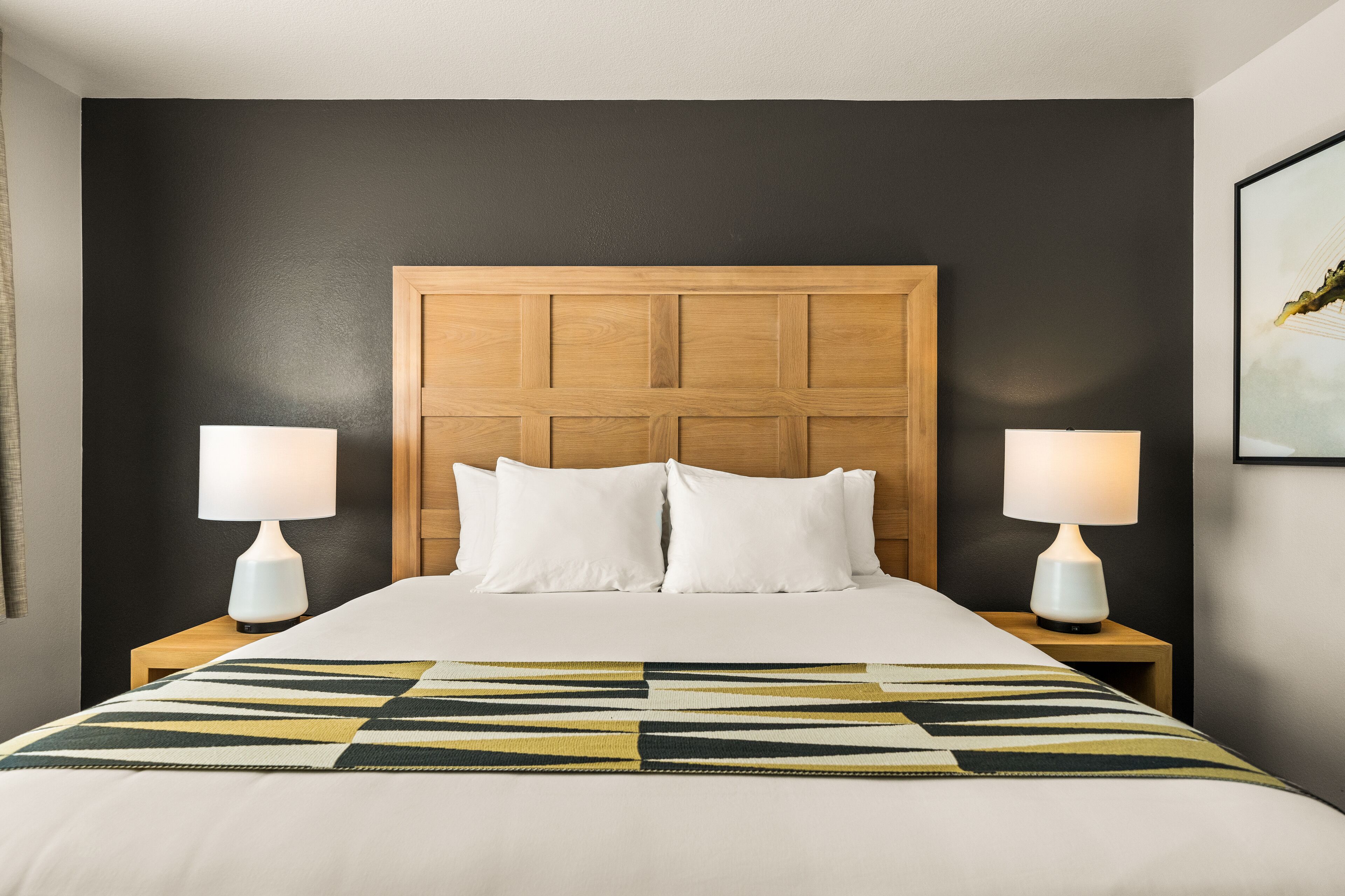 Een hotelkamer met een groot bed, twee bedlampen, een houten hoofdbord en een geborduurde plaid.