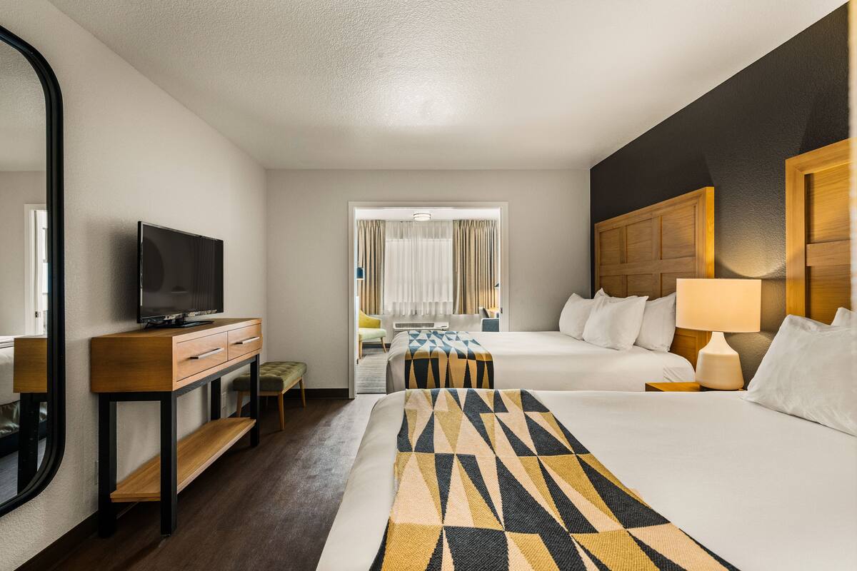 A hotel room with a bed, a desk with a TV, a window with curtains, and a nightstand with a lamp.