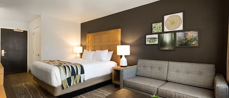 Una habitación de hotel con una cama, un sofá, una mesa de centro y una planta pequeña.
