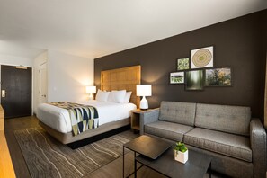 A hotel room with a bed, a sofa, a coffee table, and a small plant. - Oxford Suites Redding (Redding)