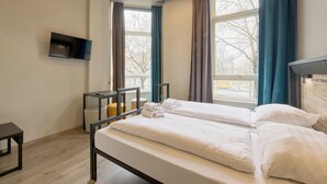 A hotel room with a bed, a TV mounted on the wall, and a window with curtains. - a&o Rotterdam City (Rotterdam)
