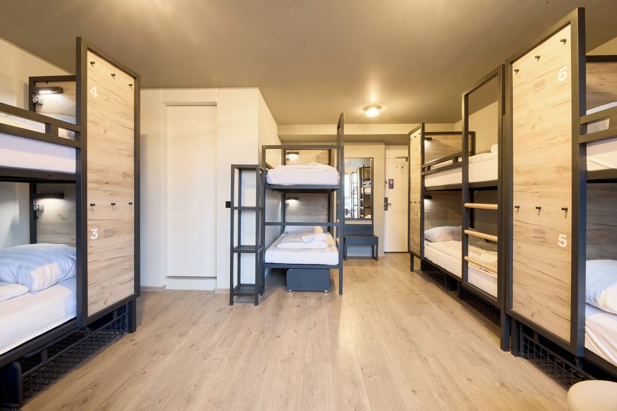 A hotel room with bunk beds, a wooden floor, and a door.