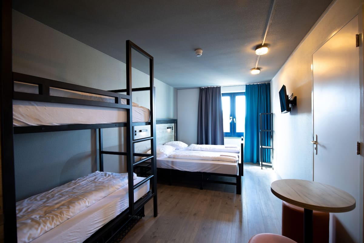 A room with bunk beds, a small table, and a window with curtains.