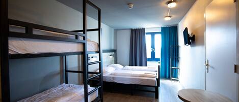Ein Zimmer mit Etagenbetten, einem kleinen Tisch und einem Fenster mit Vorhängen.