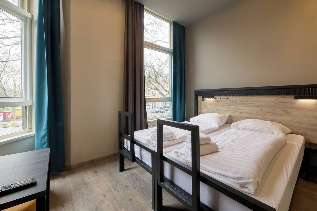 A single bed with a wooden headboard, a bedside table, and a window with curtains.