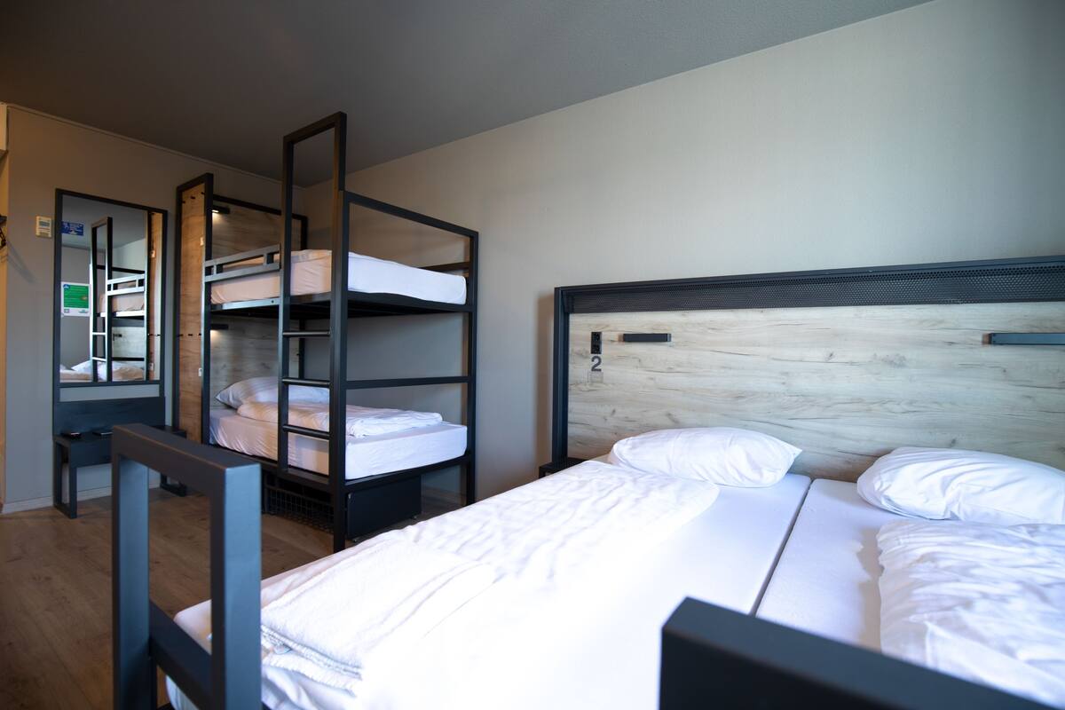A room with bunk beds, a desk, and a bed with white bedding.