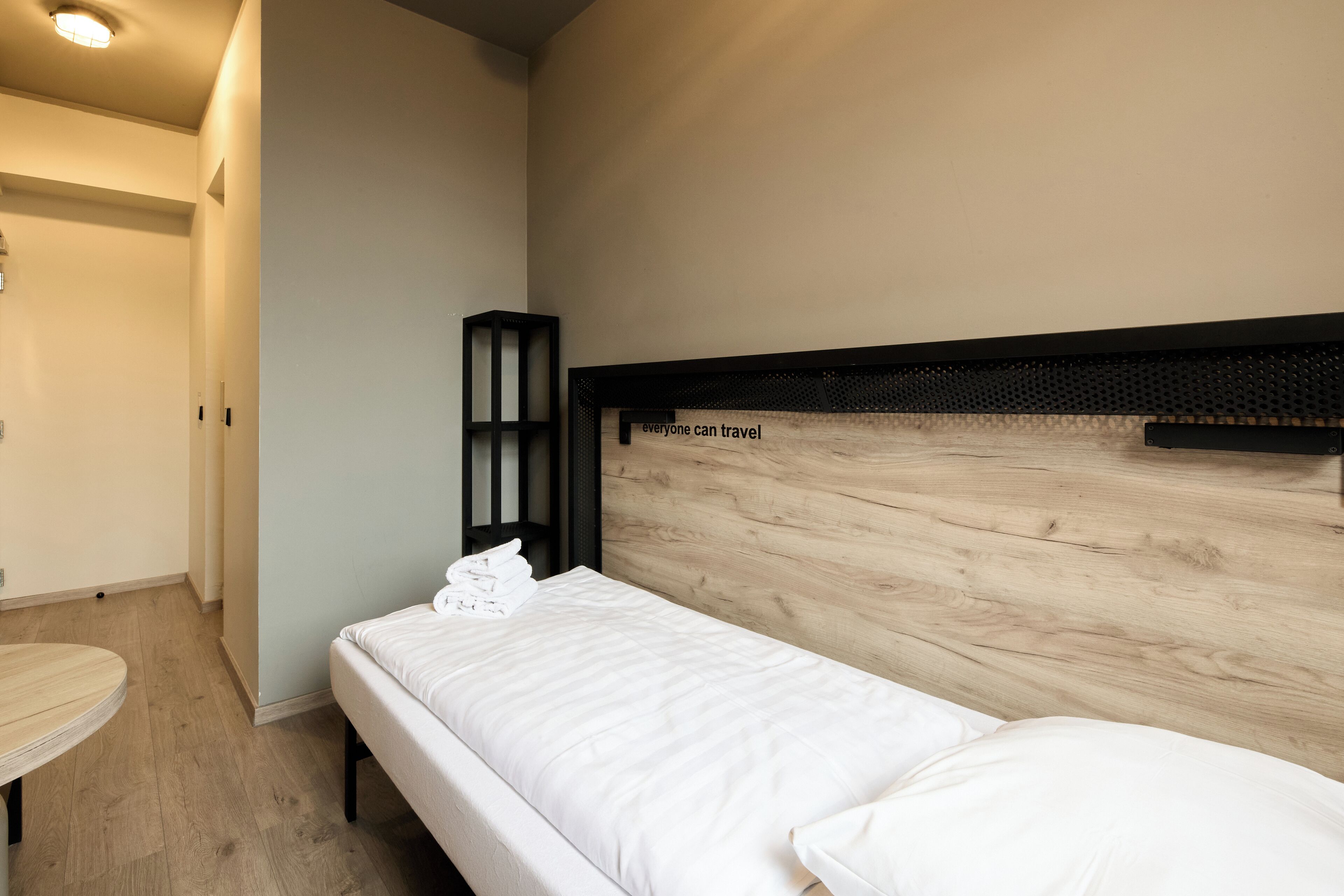 A single bed with a wooden headboard, a bedside table, and a wall-mounted shelf.