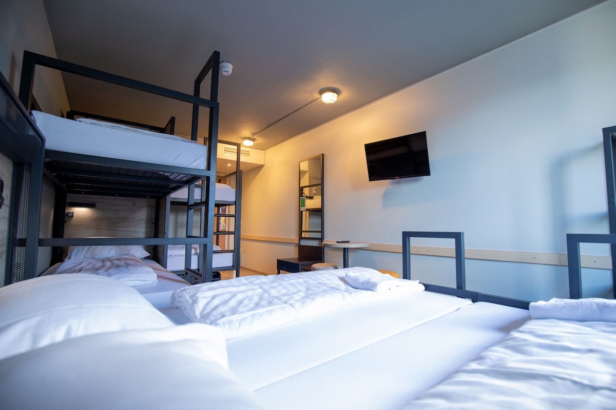 A hotel room with bunk beds, a flat-screen TV, a desk, and a mirror.