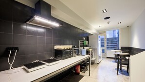 A modern kitchen with black tiled walls, a stainless steel countertop, and a built-in oven. - a&o Rotterdam City (Rotterdam)
