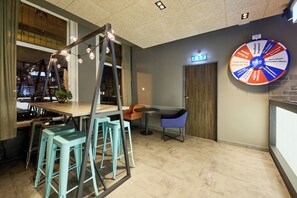 A modern interior with a bar area, teal stools, a blue chair, and a wall with a colorful circular sign.
